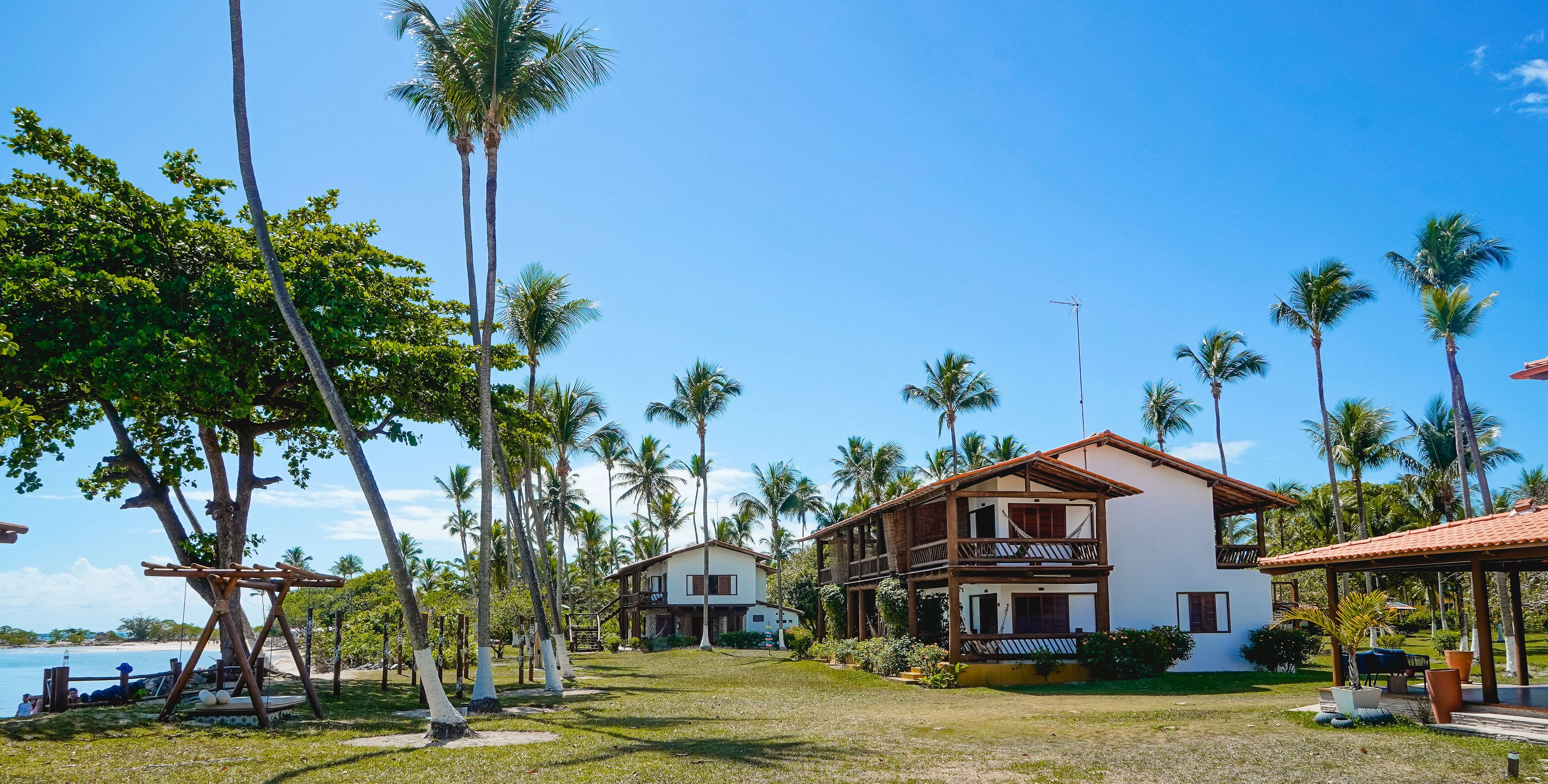 Una casa de dos pisos con balcón, rodeada de palmeras y un cielo azul despejado.