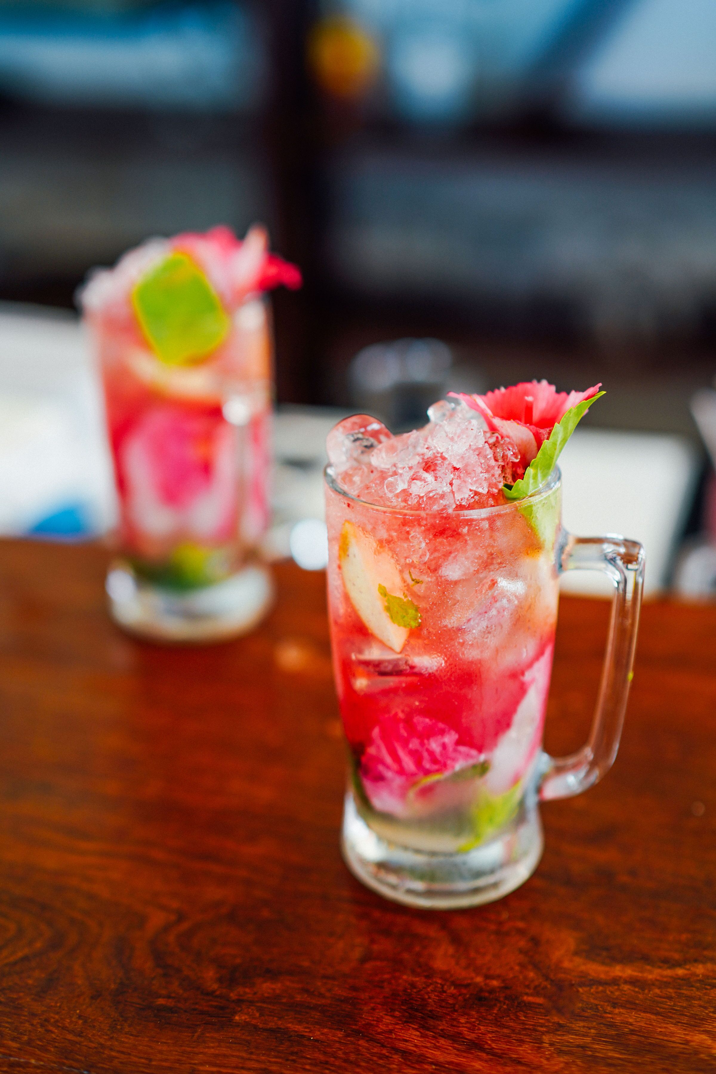 Two glasses of iced drinks with fruit garnishes on a wooden table.
