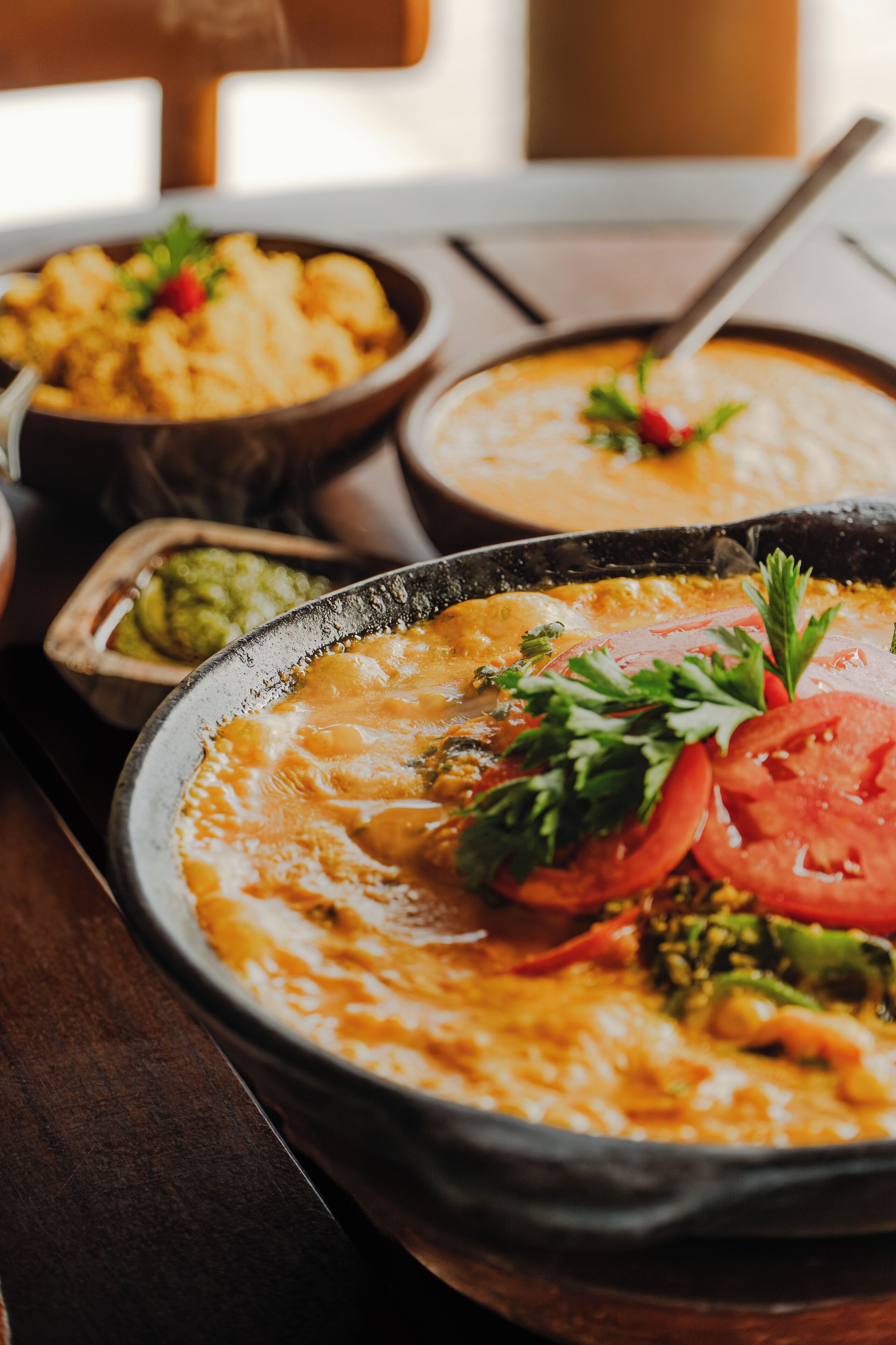 A dining table with a variety of dishes, including a bowl of soup and a plate with a slice of tomato and parsley.