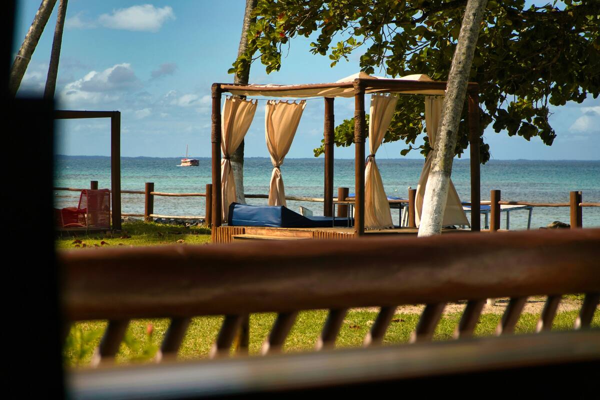 A wooden bed with a canopy, a red chair, and a view of the sea.