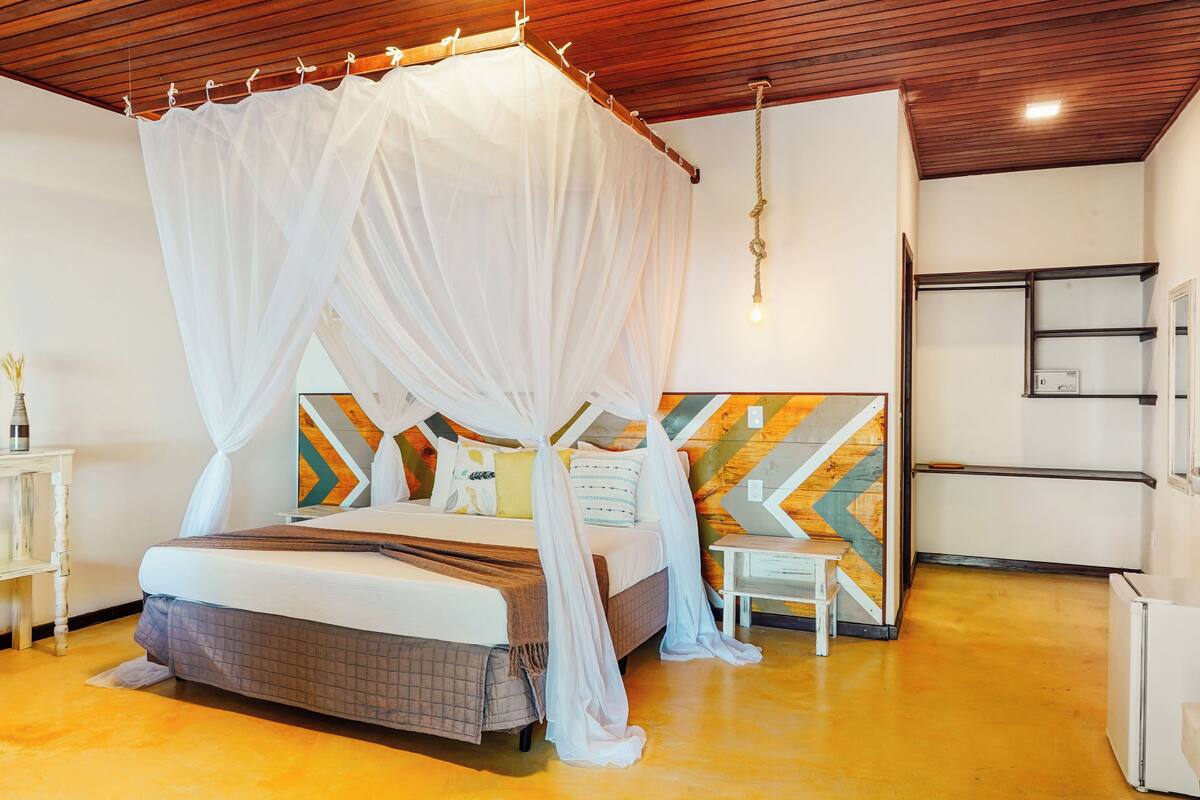 A bedroom with a canopy bed, a wooden ceiling, a geometric wall design, and a small bedside table.