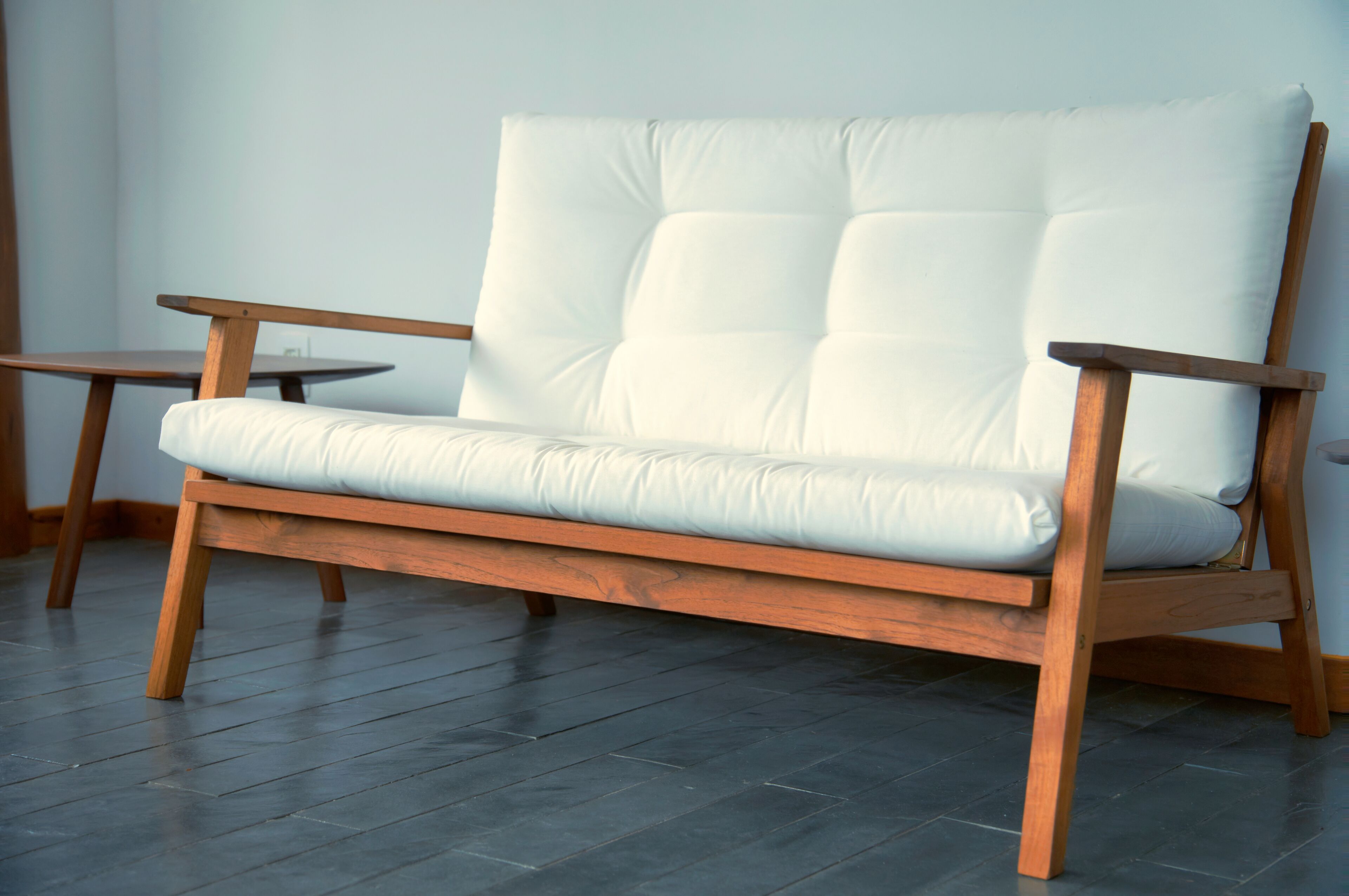 A wooden sofa with a white cushion in a room with dark wooden flooring and a plain wall.