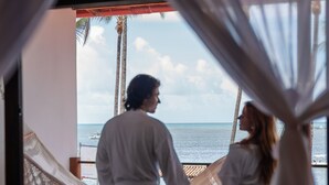 Een stel dat hand in hand staat op een balkon met uitzicht op de oceaan.