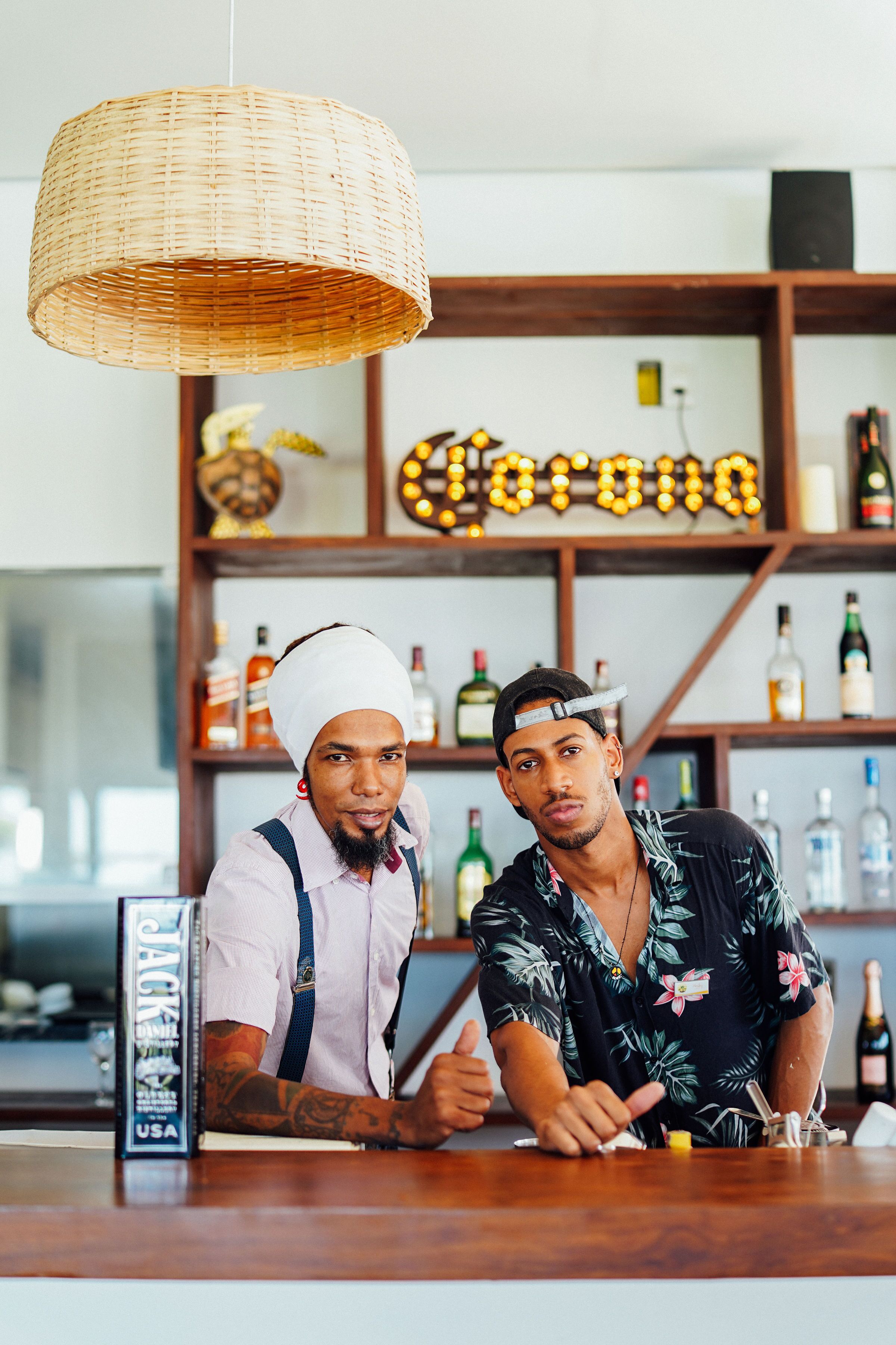 Two individuals at a bar counter with a bottle of Jack Daniel's whiskey and a sign that reads "Corona" in the background.
