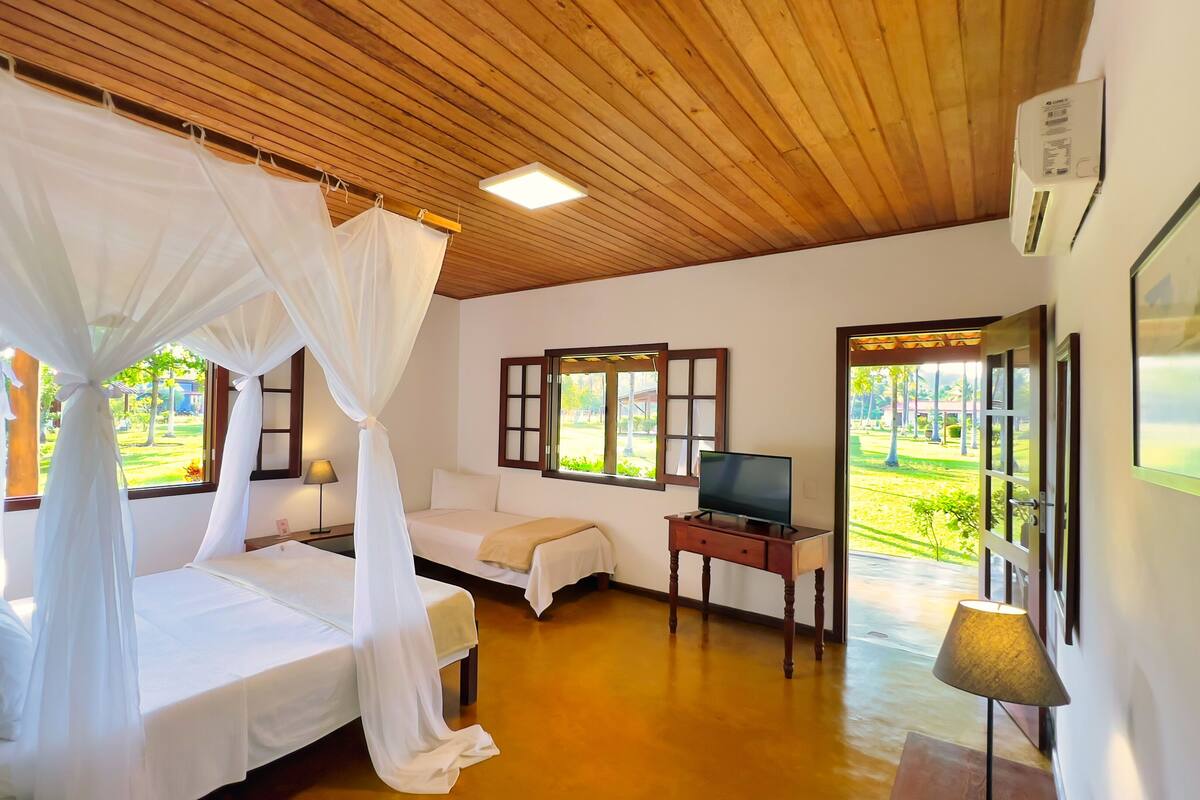 A room with a bed, a TV, a lamp, and a window with a view of greenery.