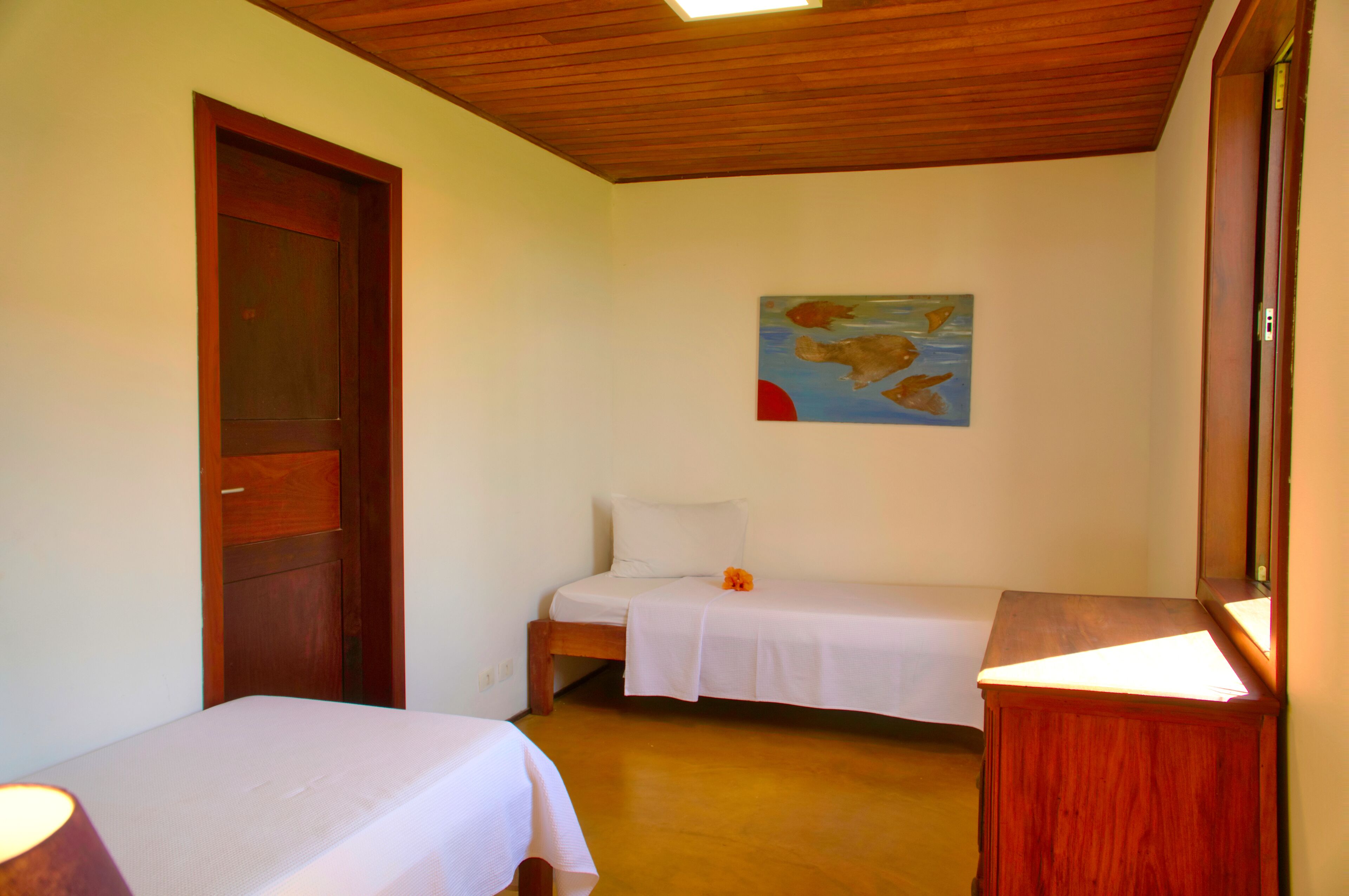 Ein Schlafzimmer mit zwei Einzelbetten, einer Holztür, einem Gemälde an der Wand und einem Nachttisch.