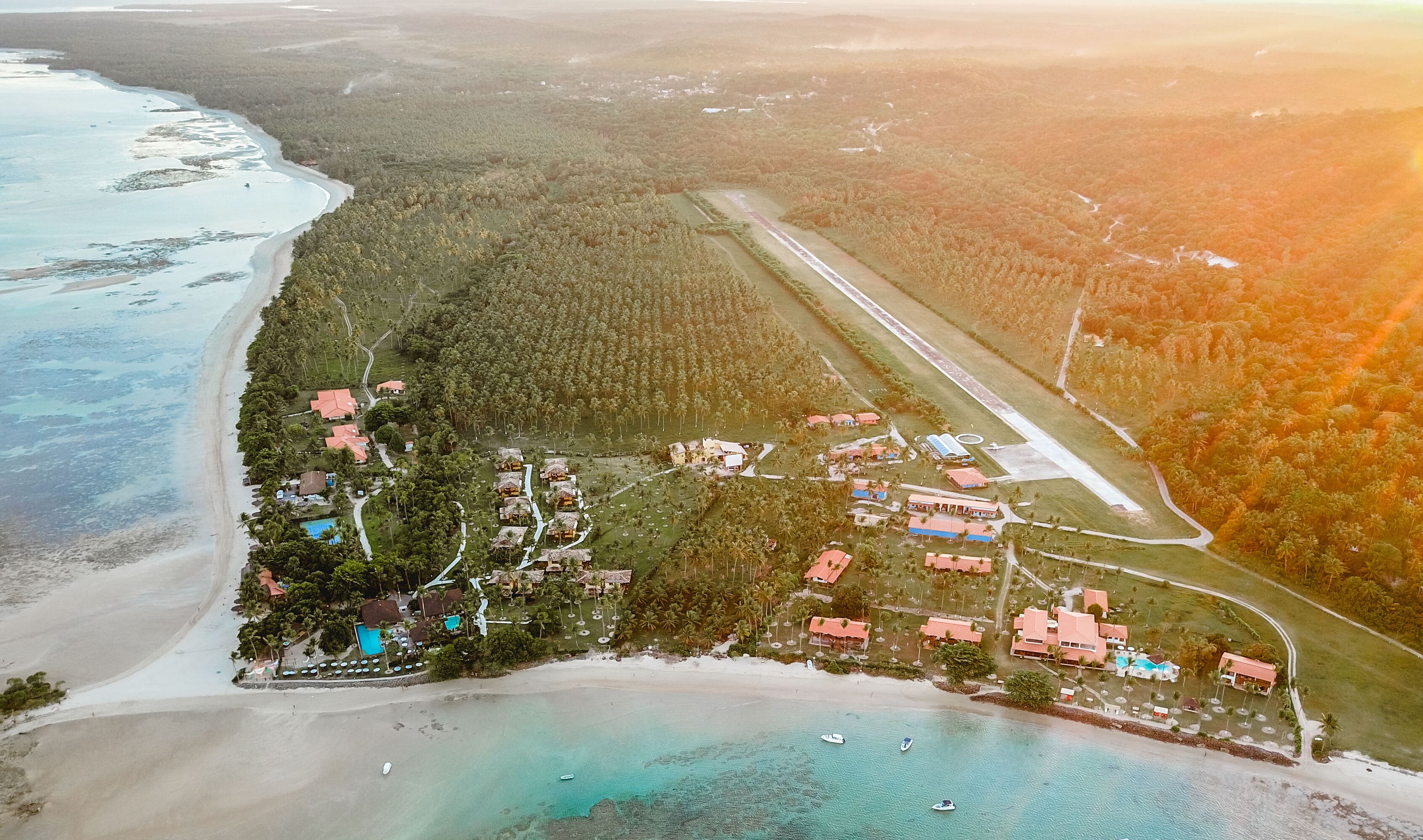 An aerial view of a coastal resort with beachfront properties, a runway, and dense forested areas.