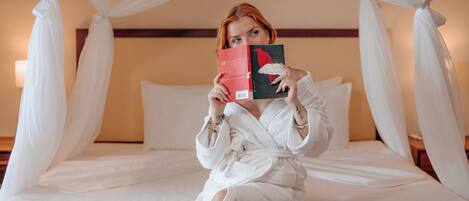 A person sitting on a bed with a canopy, holding a book.
