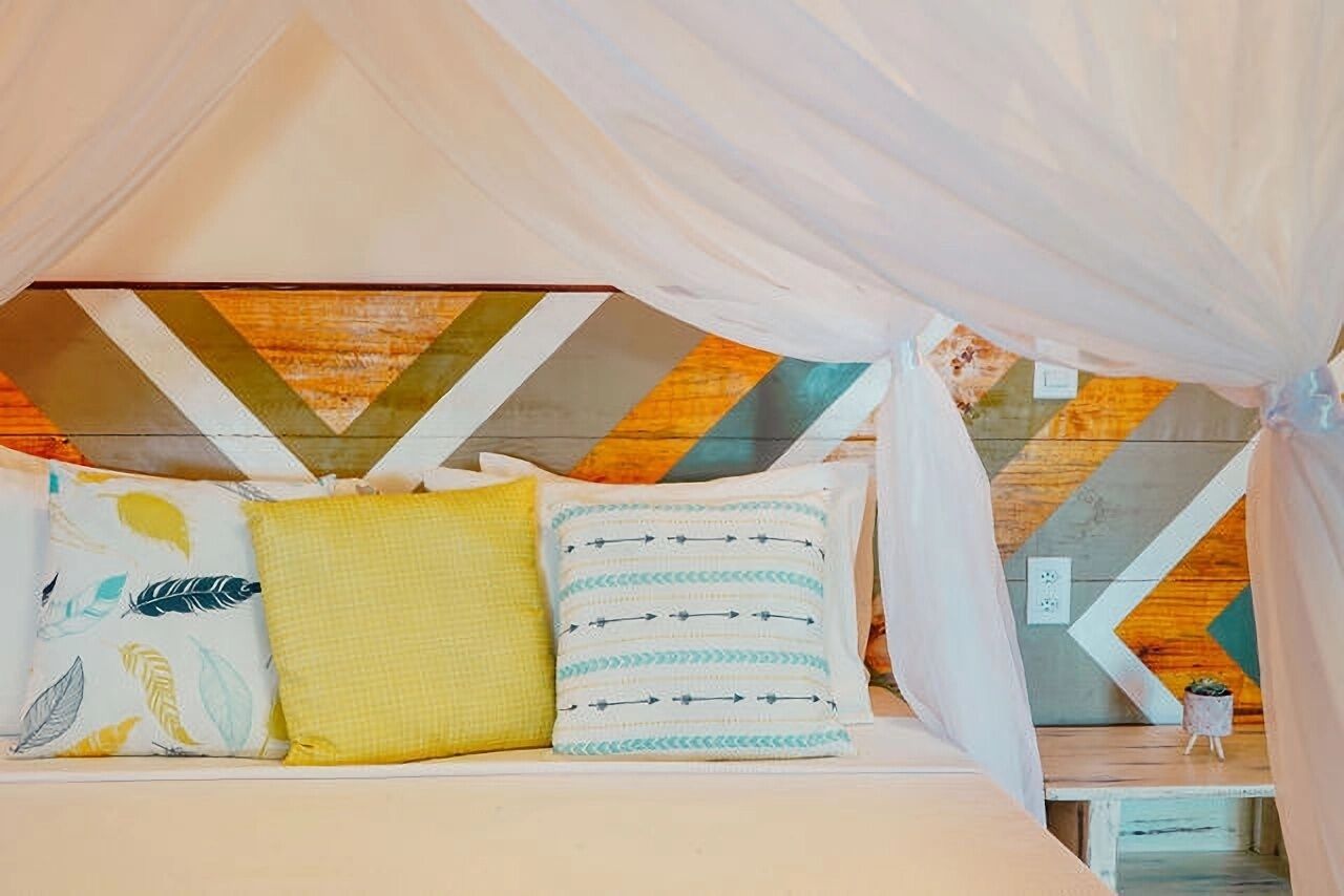 A bed with a canopy, pillows with patterns, and a geometric wall design.