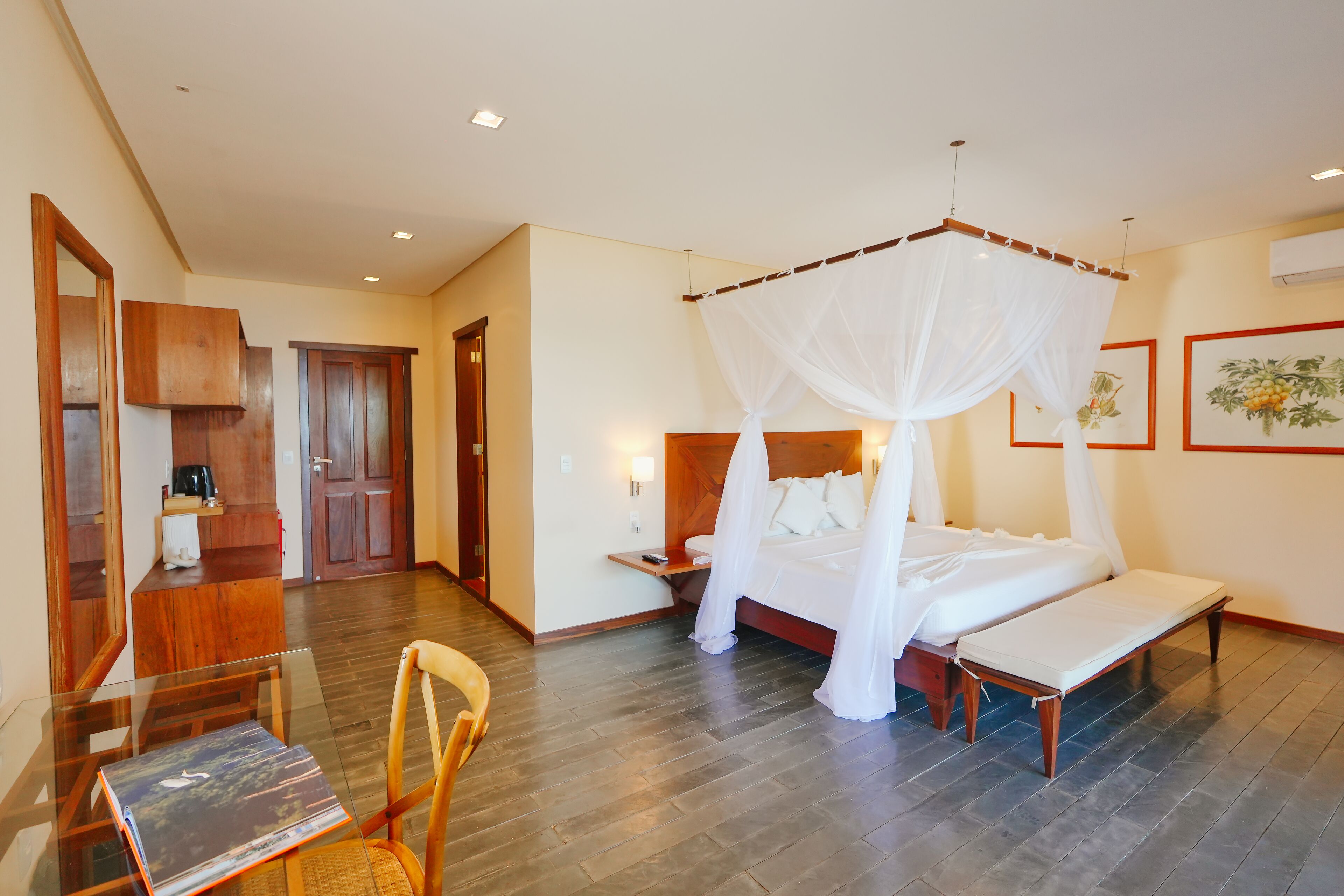 Quarto de hotel com cama de dossel, mesa de cabeceira, uma cadeira e uma pequena escrivaninha com cadeira.