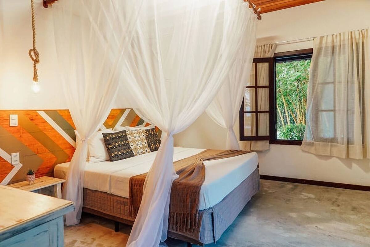 A room with a bed under a canopy, a window with curtains, and a wall with a geometric pattern.