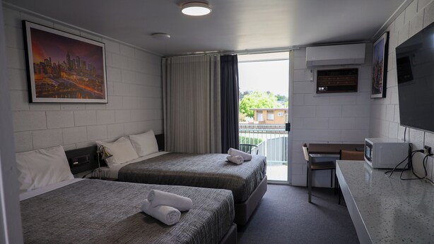 A hotel room with two beds, a desk, a television, and a cityscape painting. - Bendigo Motor Inn (Kangaroo Flat)