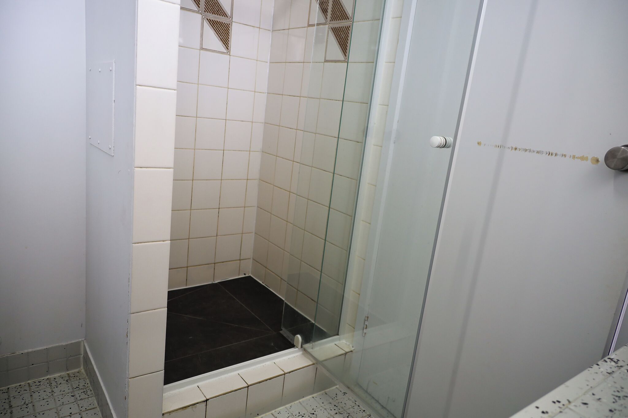 Un área de ducha pequeña y cerrada, con paredes de azulejos blancos y una puerta de vidrio.
