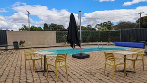 A pool area with a table and chairs, a covered umbrella, and a blue lounge chair.