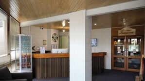 A reception area with a wooden reception desk, a refrigerator with beverages, a clock on the wall, and a sign for Medora's Restaurant. - Bendigo Motor Inn (Kangaroo Flat)