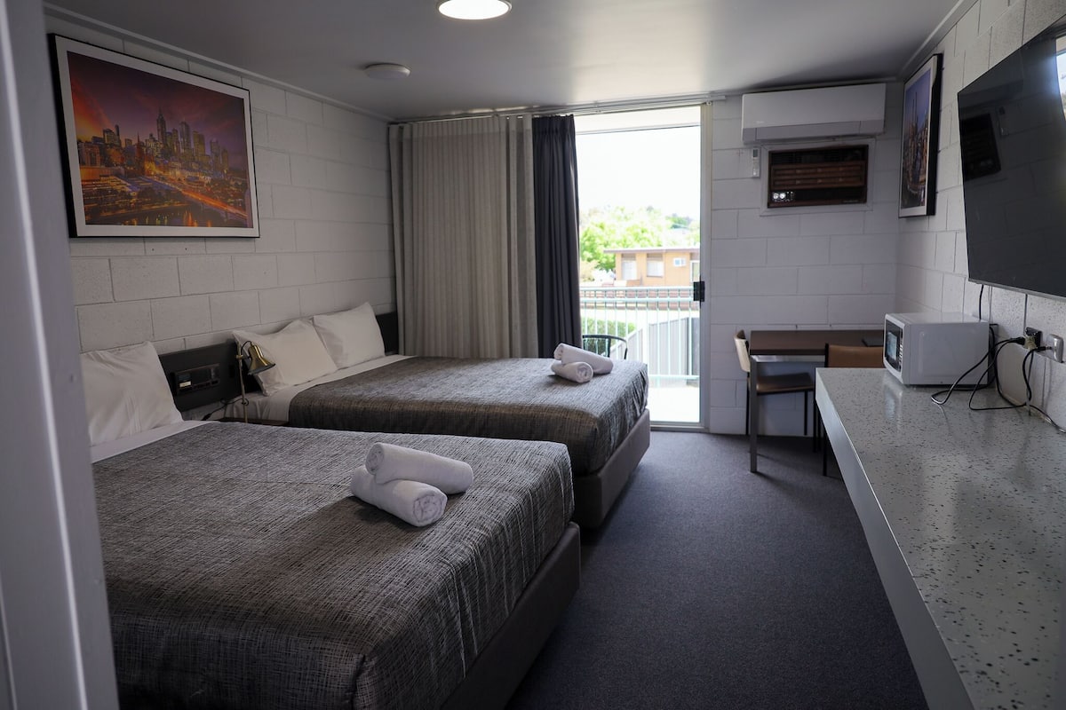 Habitación de hotel con dos camas, un escritorio, un televisor y una pintura de paisaje urbano.