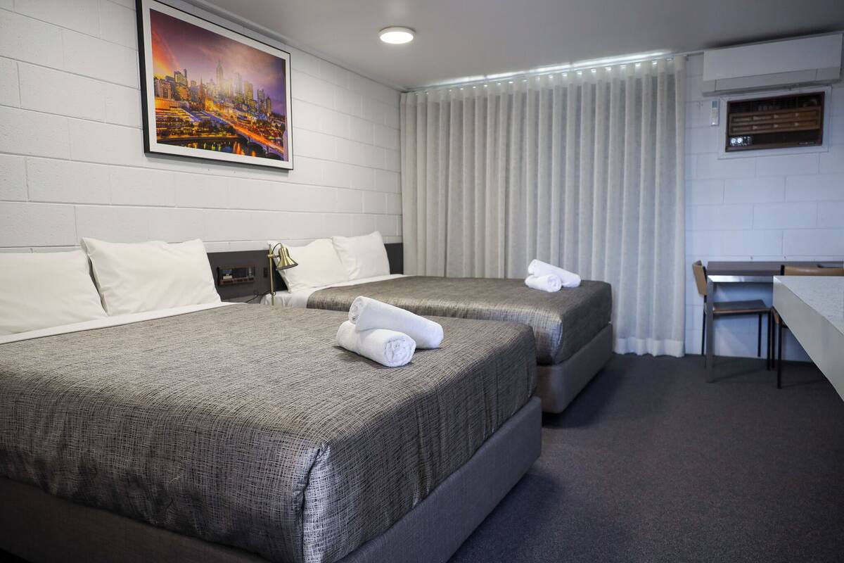 Habitación de hotel con dos camas, un escritorio y un cuadro de un paisaje urbano en la pared.