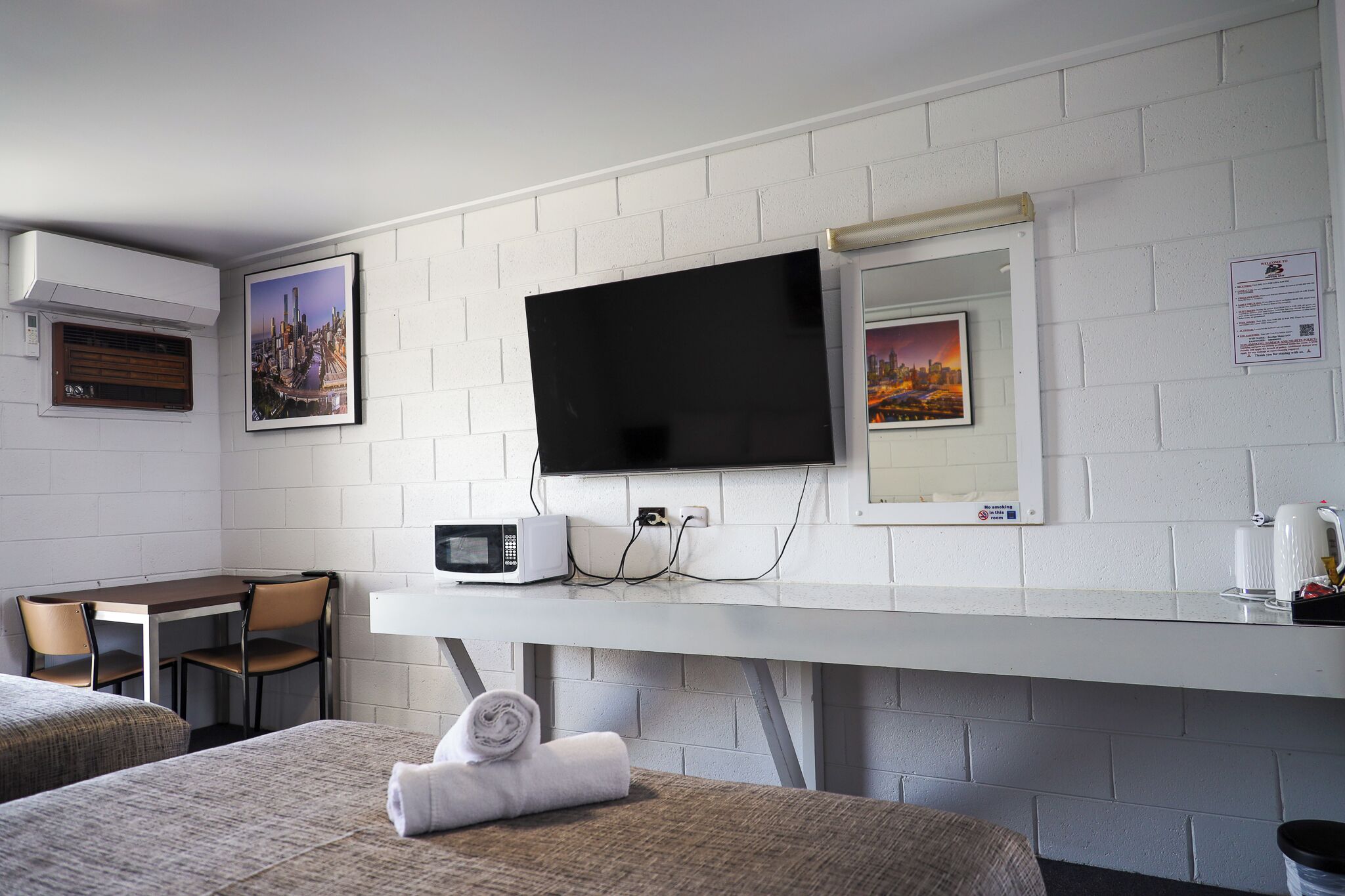 A hotel room with a bed, a desk with a chair, a TV mounted on the wall, and two framed pictures.