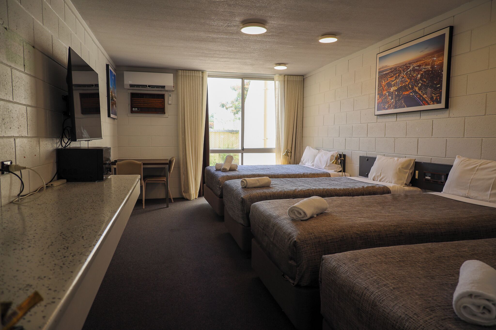 A hotel room with two beds, a desk, a TV, and a window with curtains.