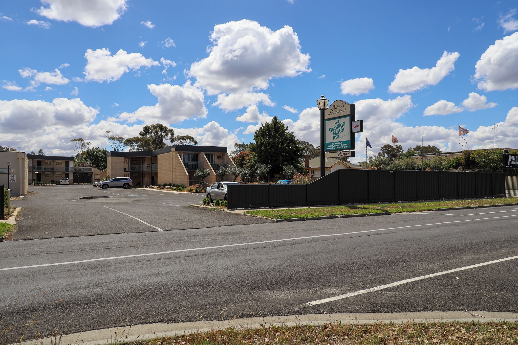 L’entrée d’un hôtel, avec une enseigne indiquant « Bendigo Motor Inn », un parking et un ciel bleu dégagé parsemé de nuages.