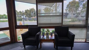 A room with two armchairs, a small table with magazines, and a view of a parking lot through large windows. - Bendigo Motor Inn (Kangaroo Flat)