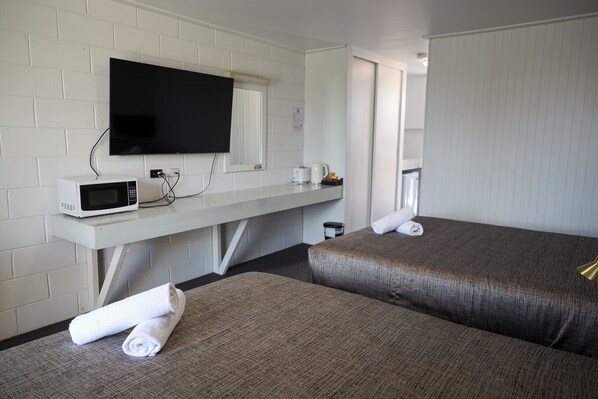 A hotel room with two beds, a TV, a microwave, and a small table with a kettle and cups.