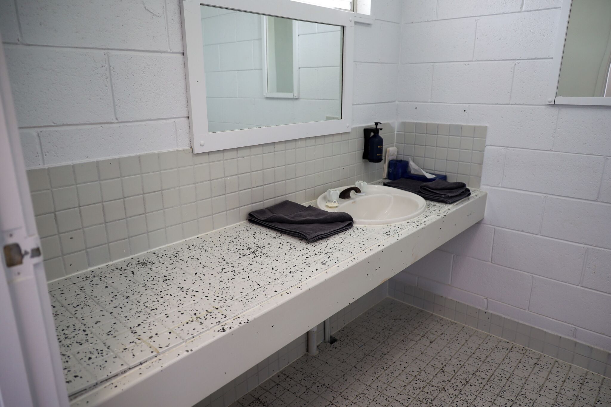 A public restroom with a white tiled wall, a single sink, and a mirror.