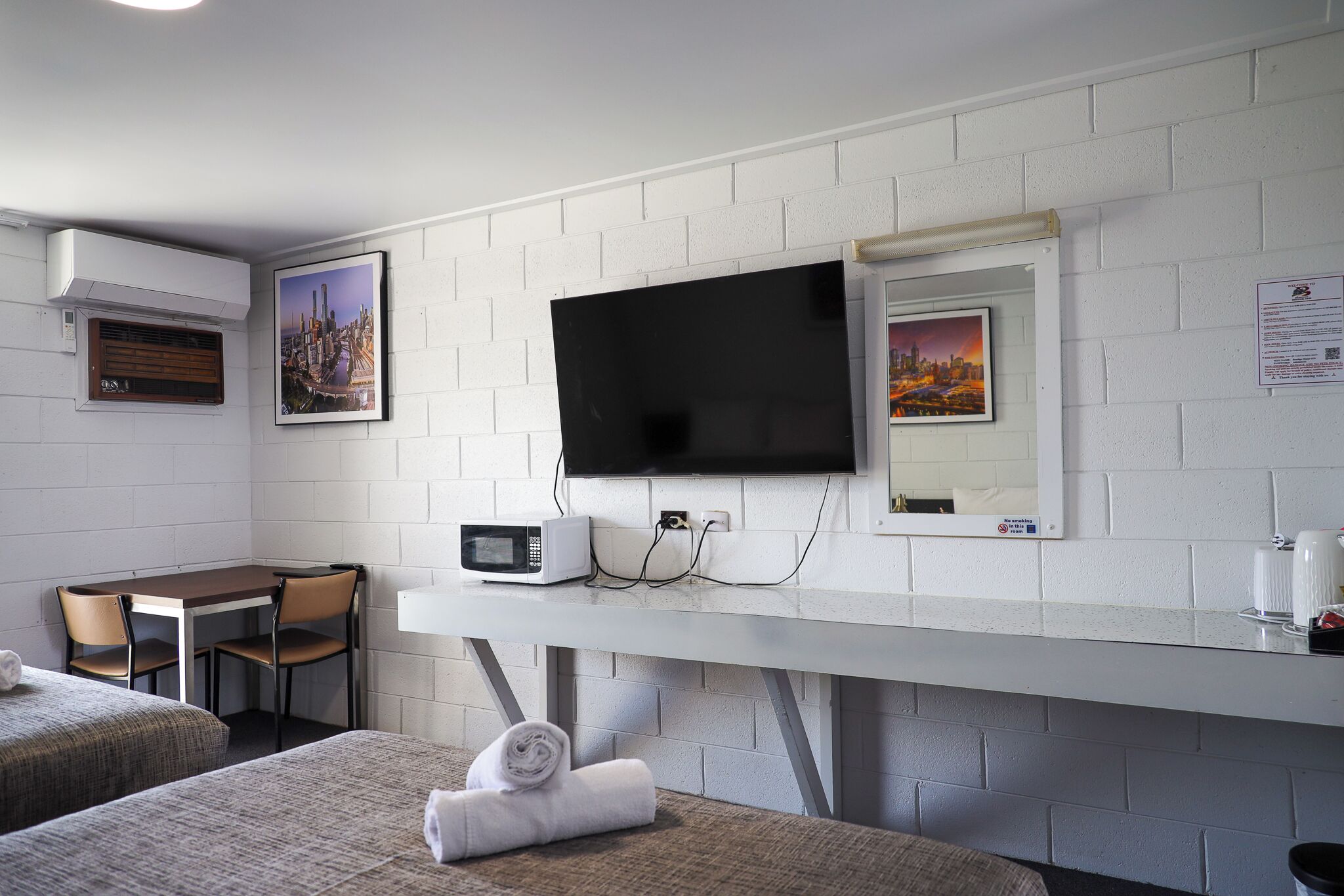Habitación de hotel con una cama, un escritorio con una silla, un televisor en la pared y un microondas sobre el escritorio.