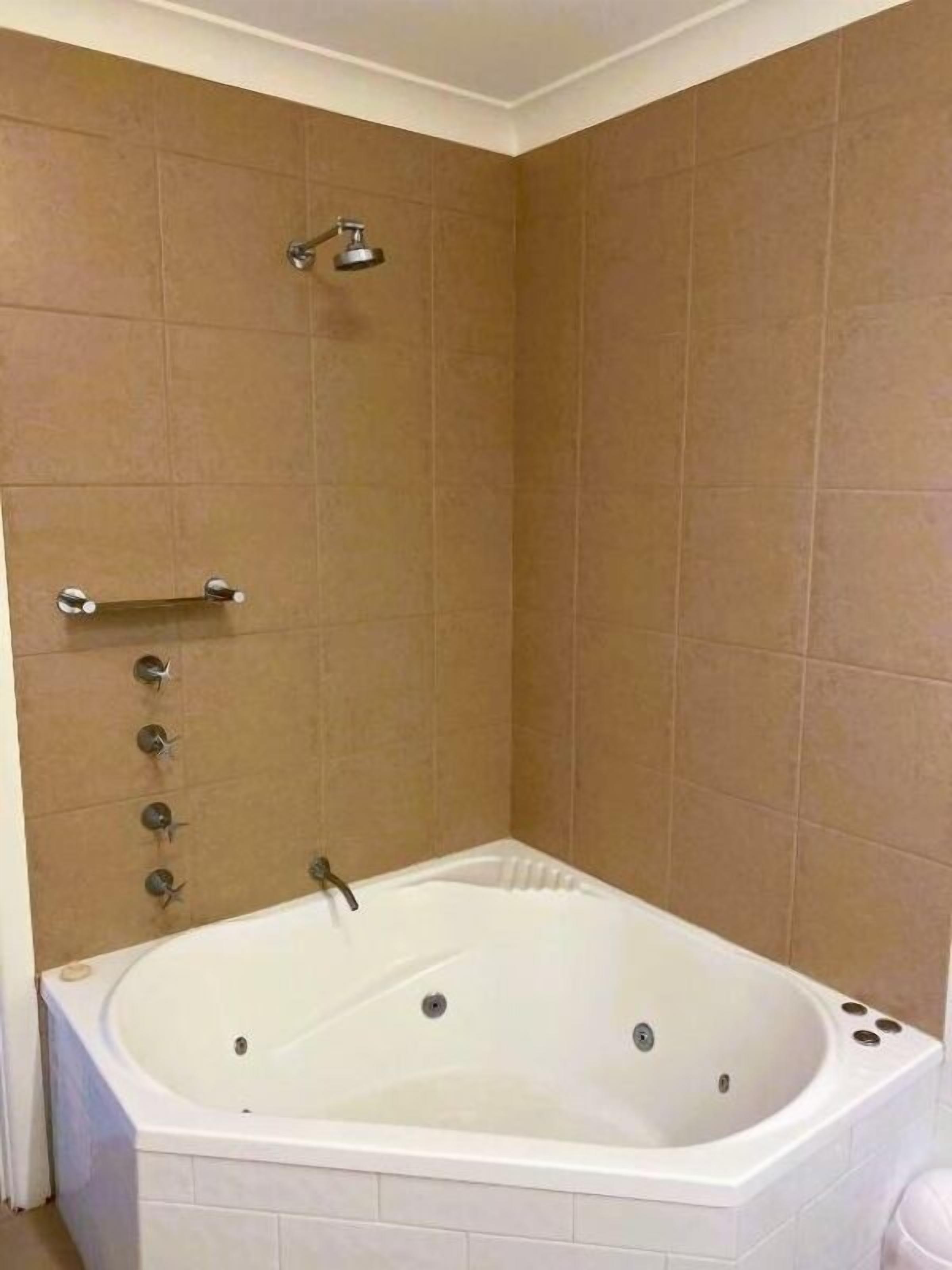 A bathroom with a large bathtub, a showerhead, and a towel rack.