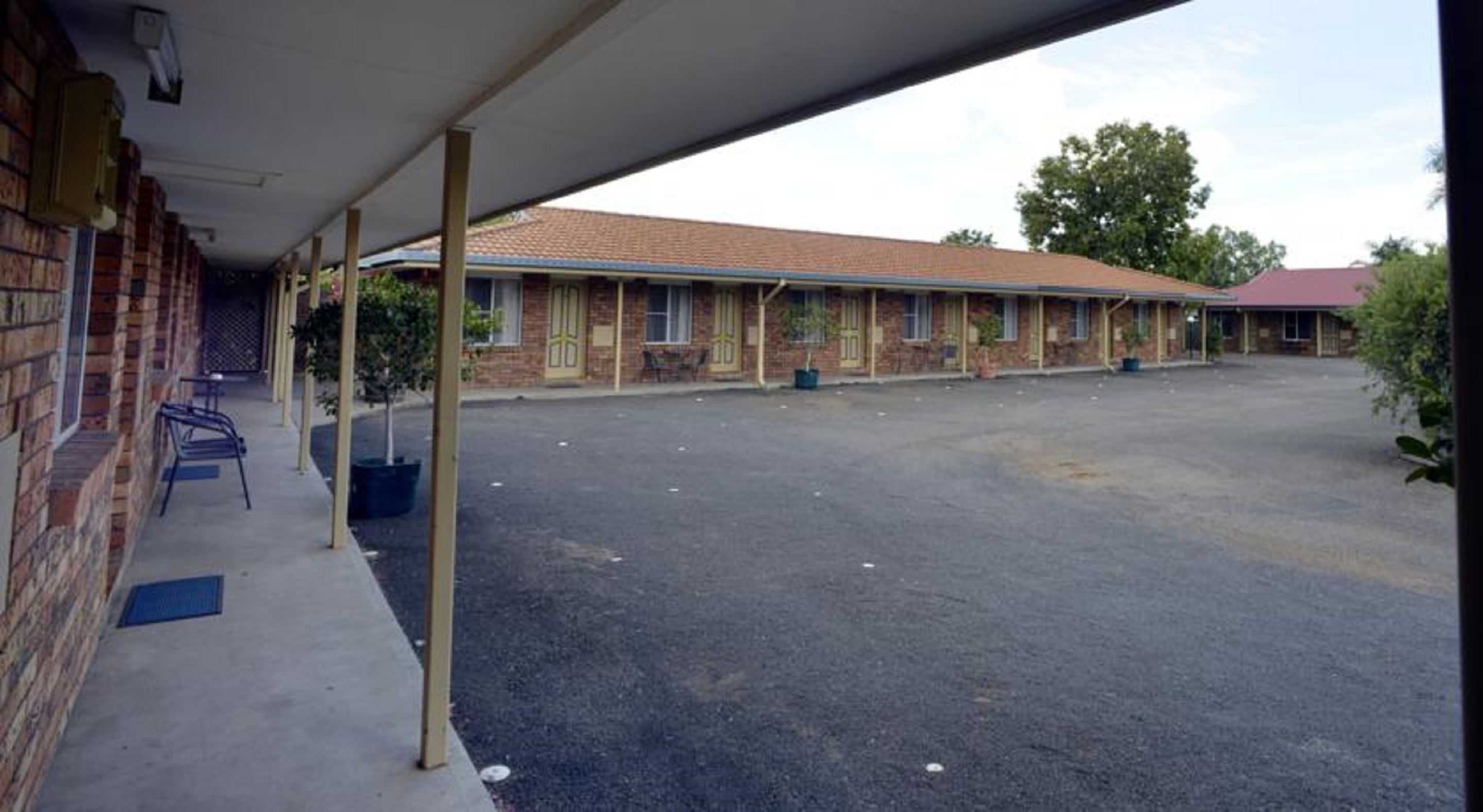 Un motel con área de estacionamiento techada, fachada de ladrillo y varias habitaciones con ventanas.