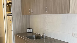 A modern kitchen with light wood cabinetry, a stainless steel sink, and a built-in oven. - Bellview Motel (Narrabri)