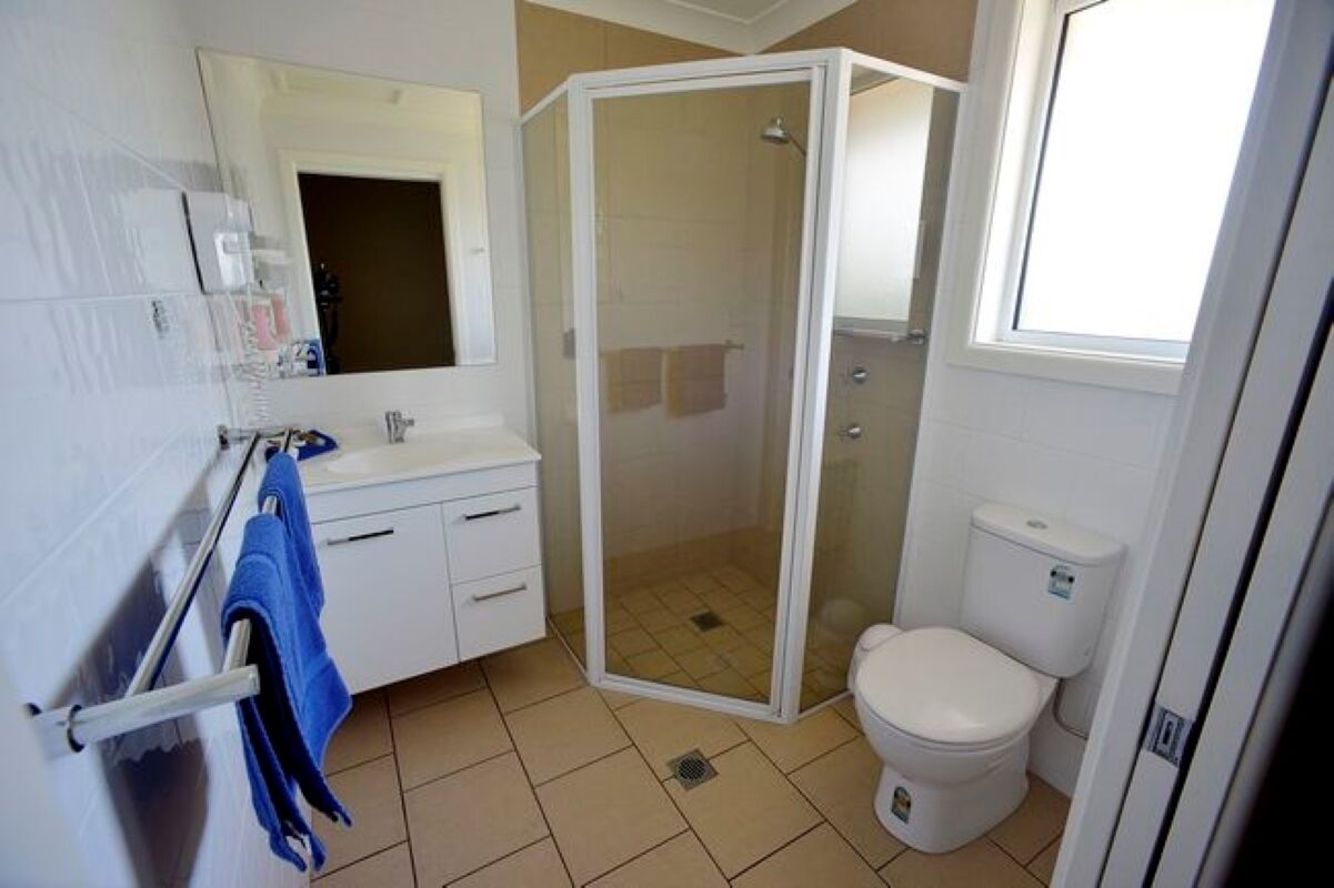 A bathroom with a shower enclosure, a toilet, a sink with a mirror, and a towel rack.