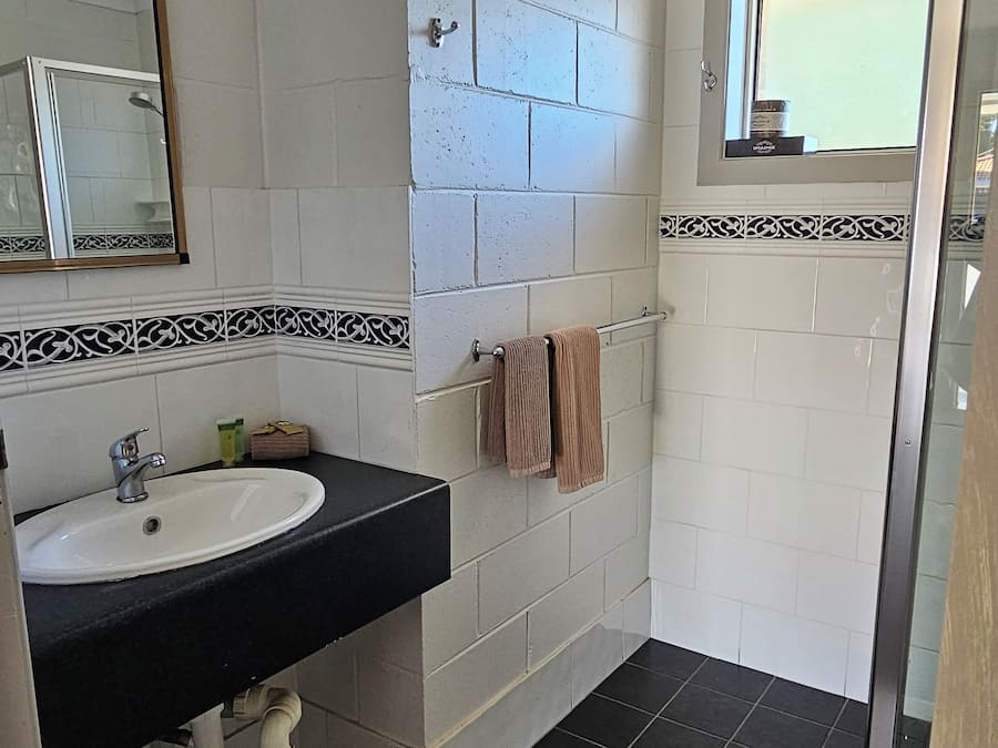 A bathroom with a white sink, black countertop, and a shower area.