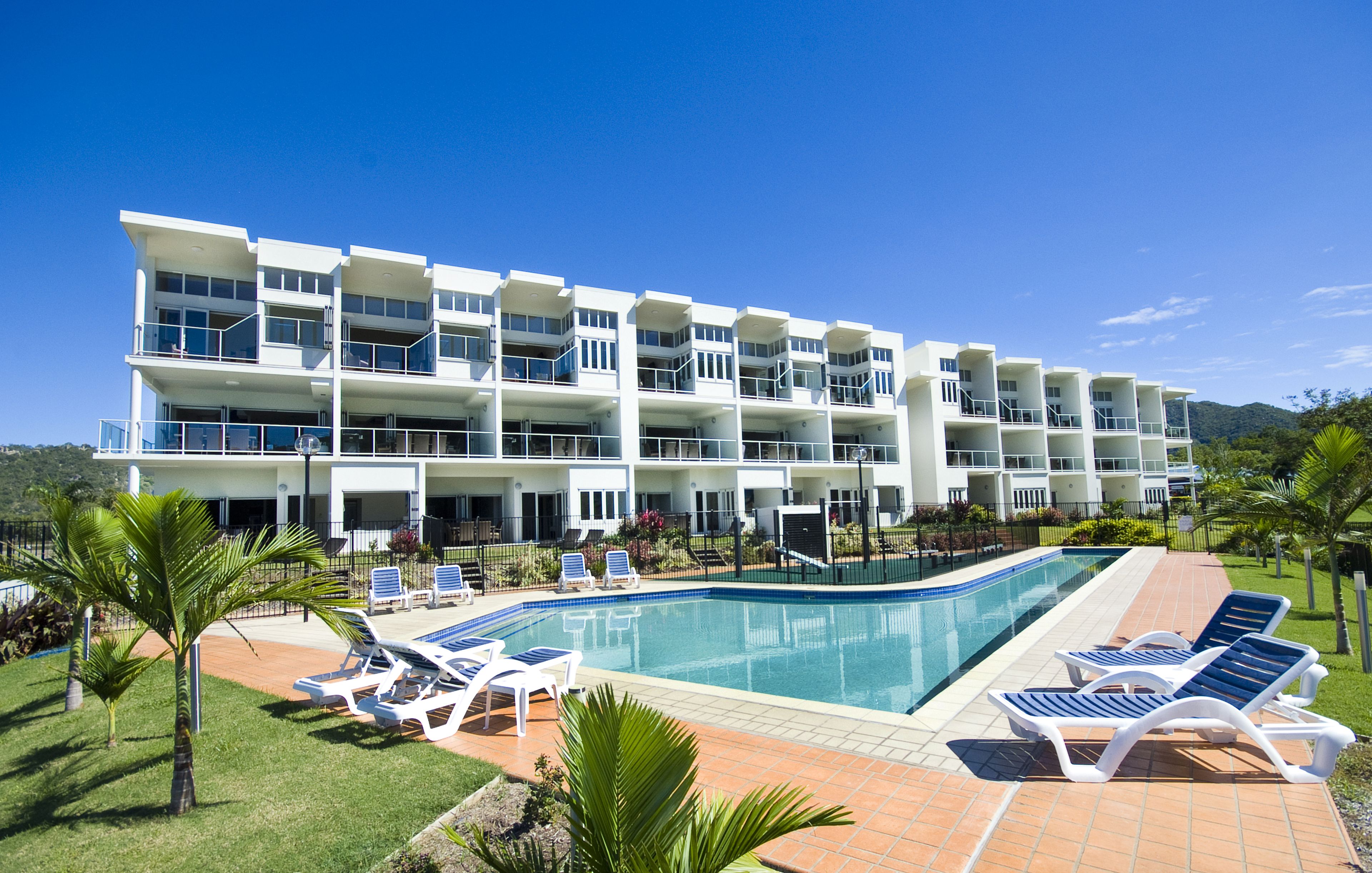 Un hotel moderno con piscina, diversi balconi e lettini prendisole.