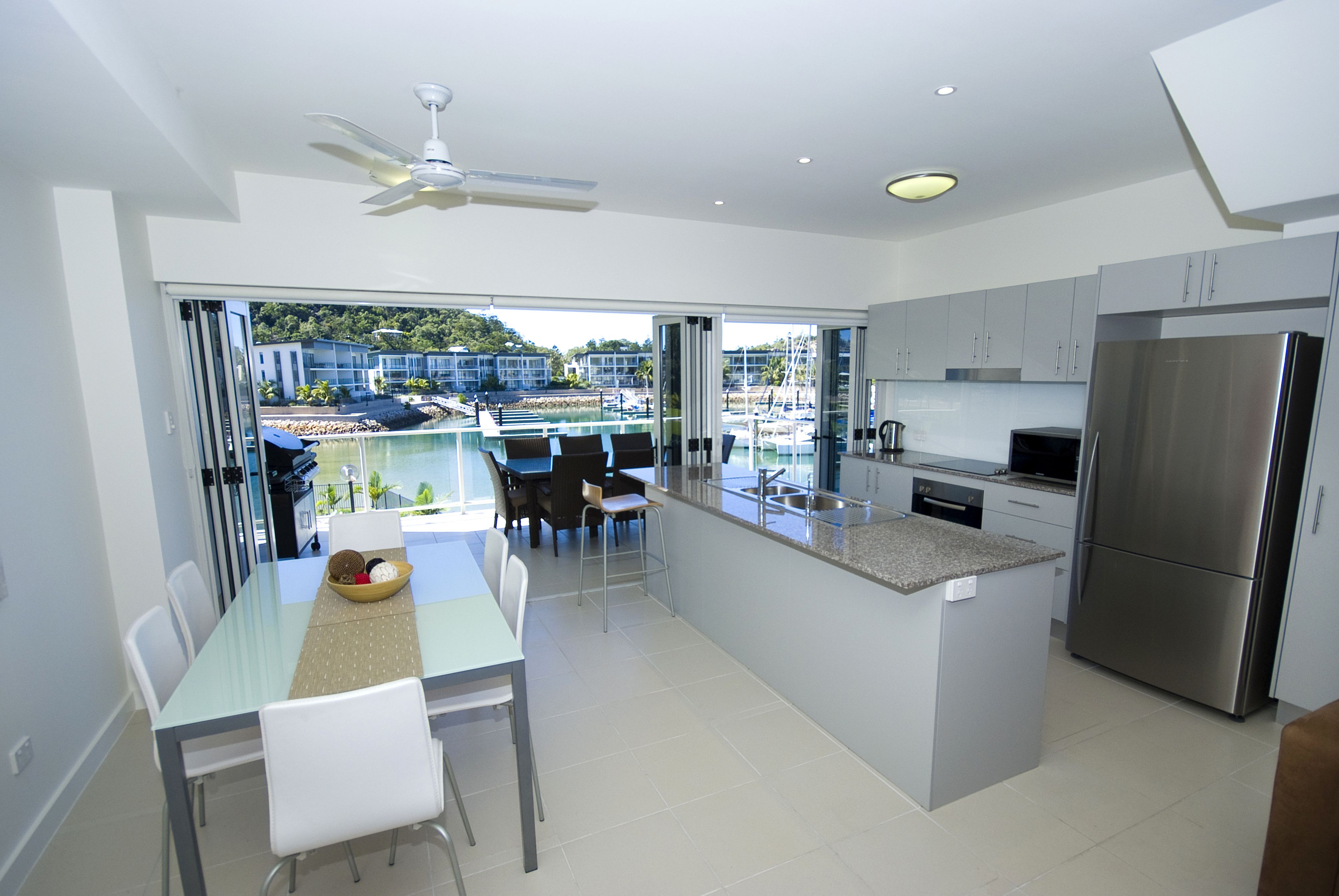 A modern kitchen with a large island, stainless steel appliances, and a dining area with a view of a pool and buildings.