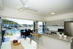 Una cocina moderna con vista a una piscina y edificios, un comedor con sillas y una mesa, y un ventilador de techo.
