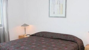 Una habitación sencilla y limpia con una cama, una lámpara y un cuadro en la pared.