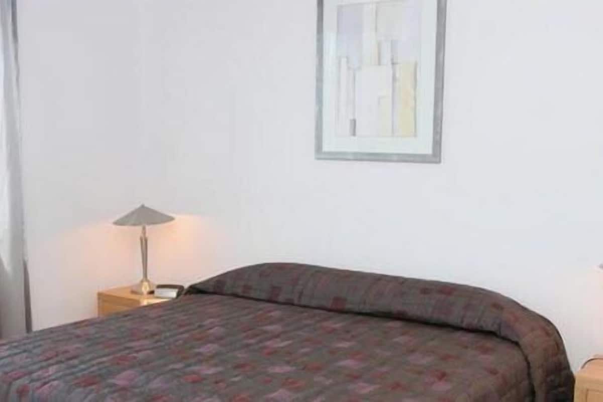 A simple, clean room with a bed, a lamp, and a framed picture on the wall.