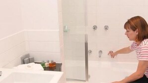 Un baño con cabina de ducha de vidrio, lavamanos con artículos de aseo y pared de azulejos blancos.
