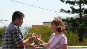 Dos personas sentadas en una mesa al aire libre con barandilla, sosteniendo copas de vino.