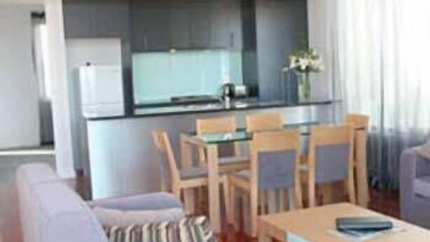 Una sala moderna con un sofá, una mesa de comedor y una zona de cocina con refrigerador y armarios.