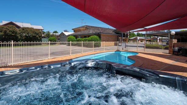 Una piscina con un jacuzzi, rodeada por una zona vallada, bajo un dosel rojo.