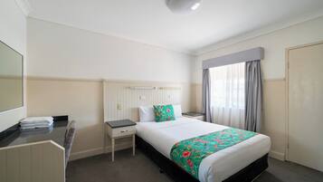 Habitación de hotel con cama, mesita de noche, escritorio con silla, espejo y ventana con cortinas.