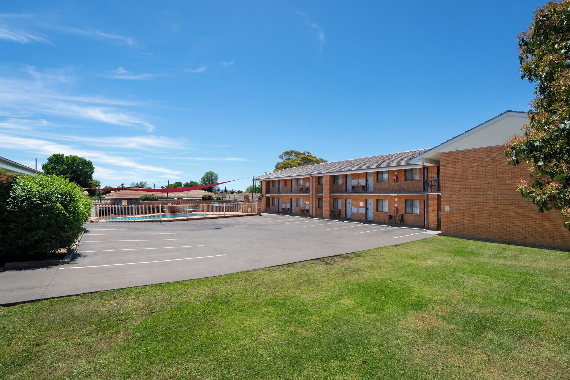 A two-story motel with a swimming pool, a parking lot, and a grassy area.