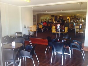A restaurant with multiple tables and chairs, a bar area in the background, and a person in a red shirt.