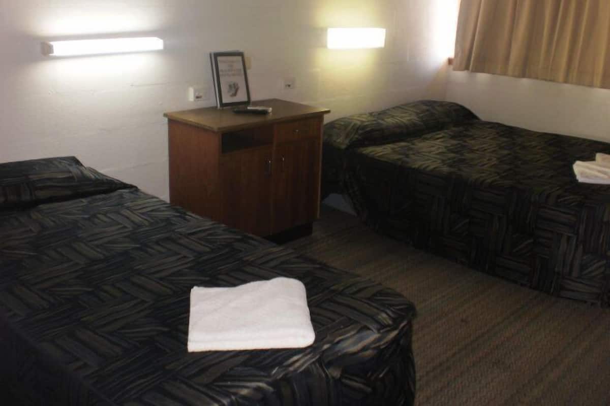 Una habitación de hotel con dos camas individuales, un aparador de madera y una mesita de noche con una lámpara.