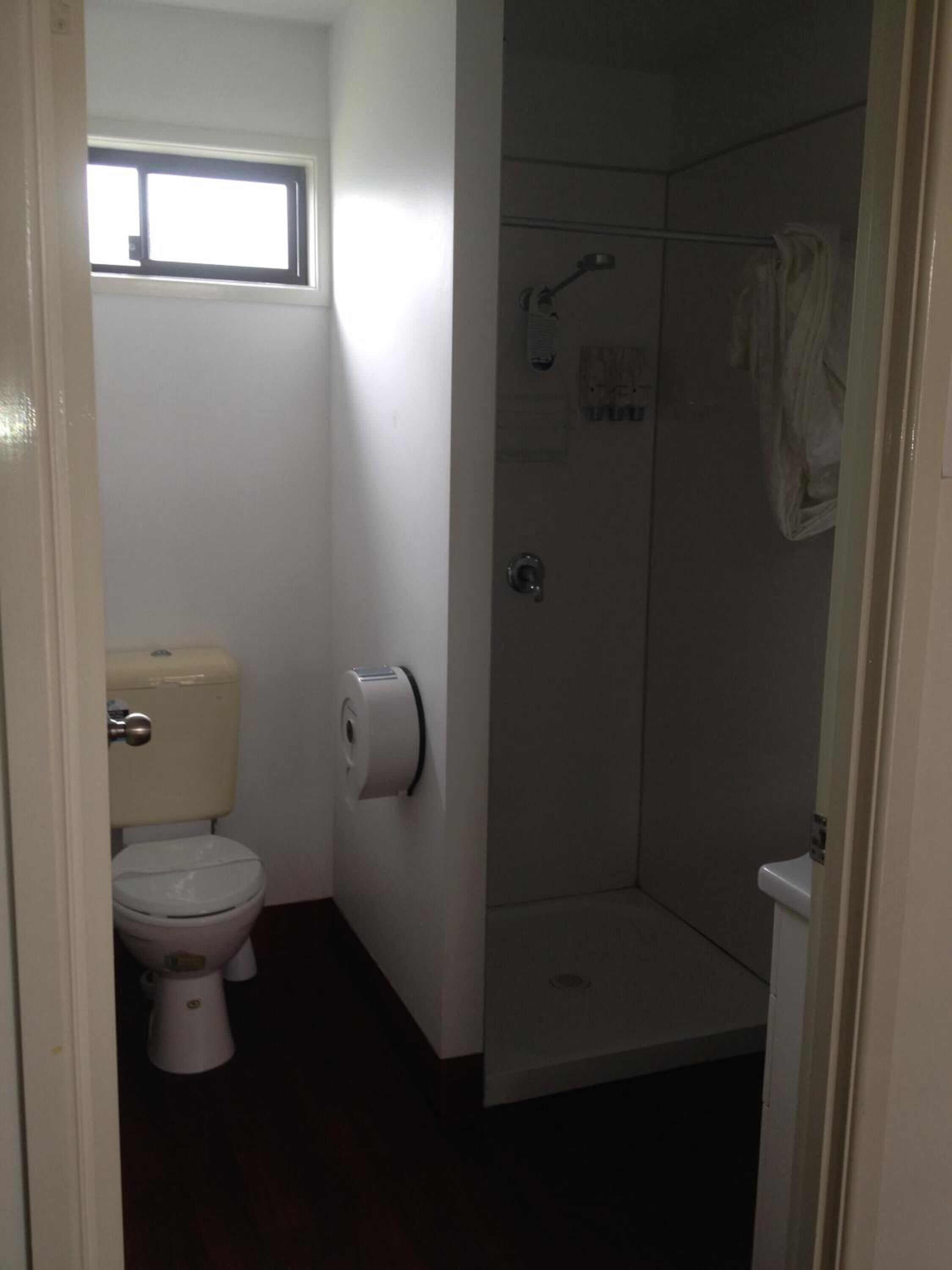 A small bathroom with a toilet, a shower stall, and a window above the toilet.