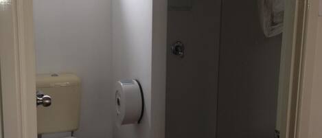 Un baño pequeño con inodoro, cabina de ducha y ventana sobre el inodoro.