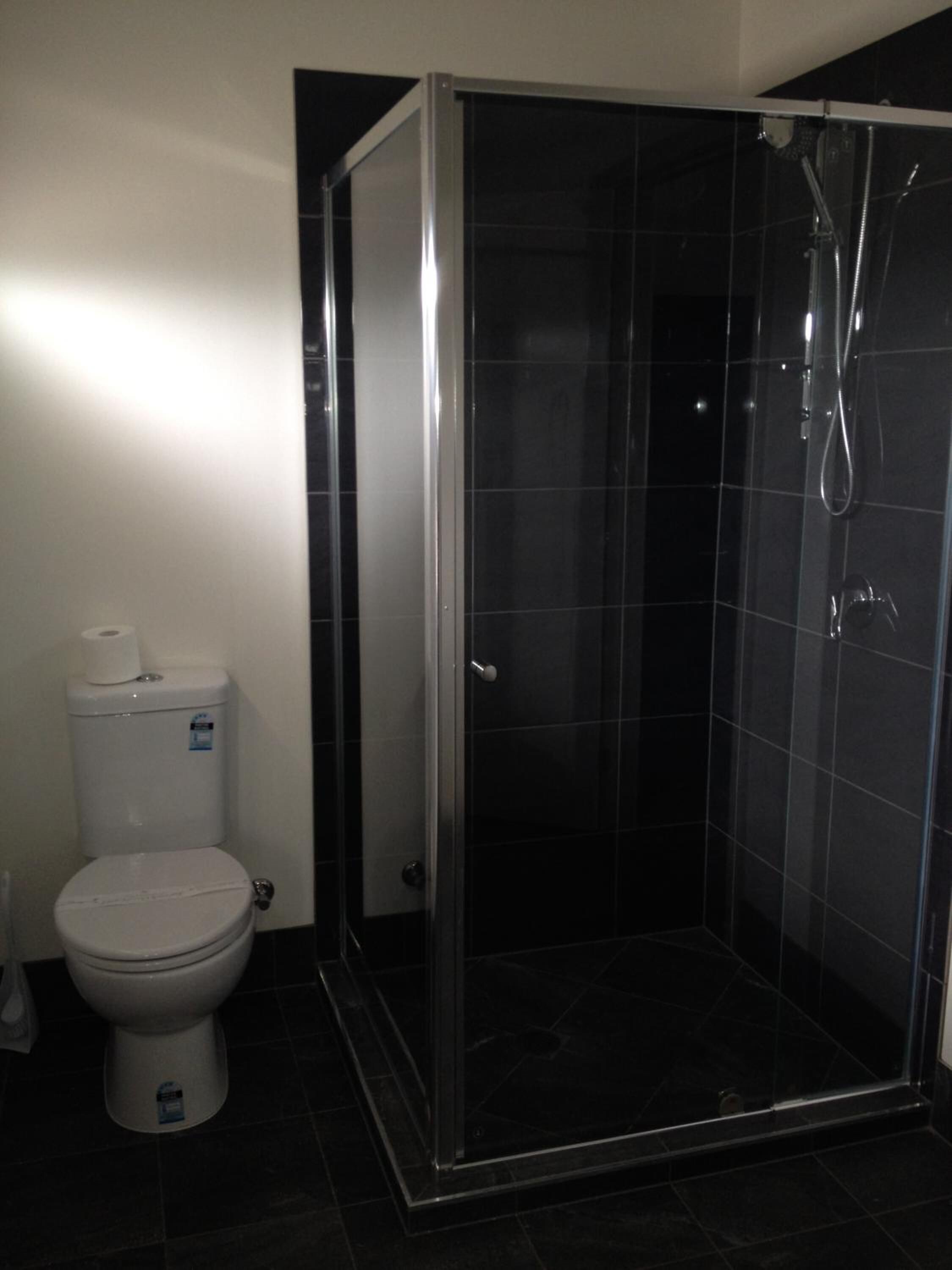 A bathroom with a toilet, a shower enclosure, and dark tiled walls.