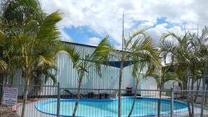 A swimming pool surrounded by a fence, with palm trees and a building in the background. - Blackwater Hotel Motel (Blackwater)